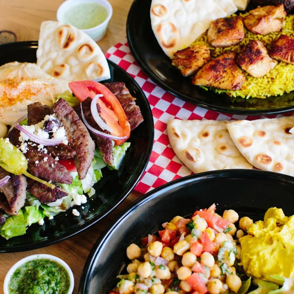 Middle Eastern meal spread featuring grilled meats, yellow rice, flatbreads, hummus, chickpea salad, and a fresh steak salad.