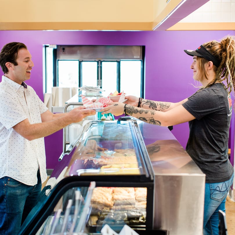 A Peno Mediterranean Grill employee serves a customer food from a display case.