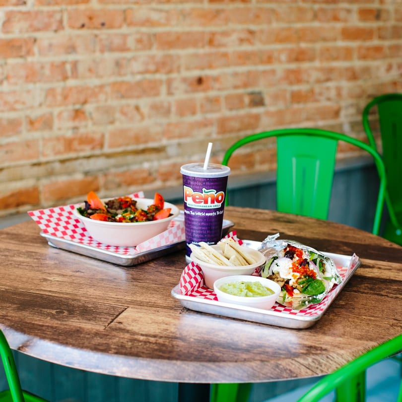 Peno Mediterranean Grill dishes on a wooden table, including a bowl, a wrap, and a drink.