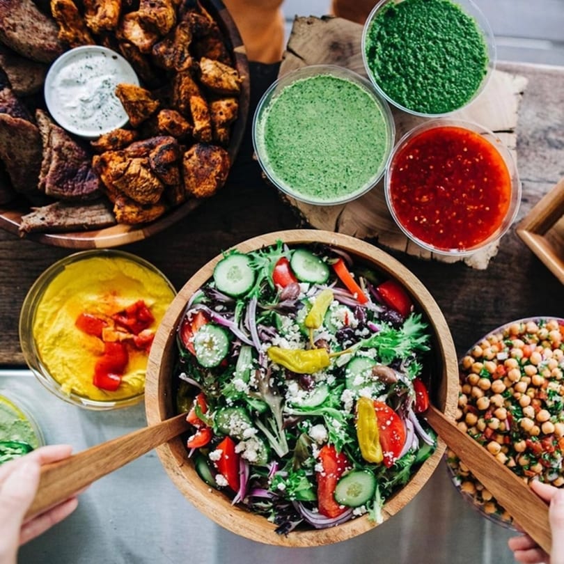 Overhead view of a Mediterranean spread with grilled meats, hummus, salads, and sauces.