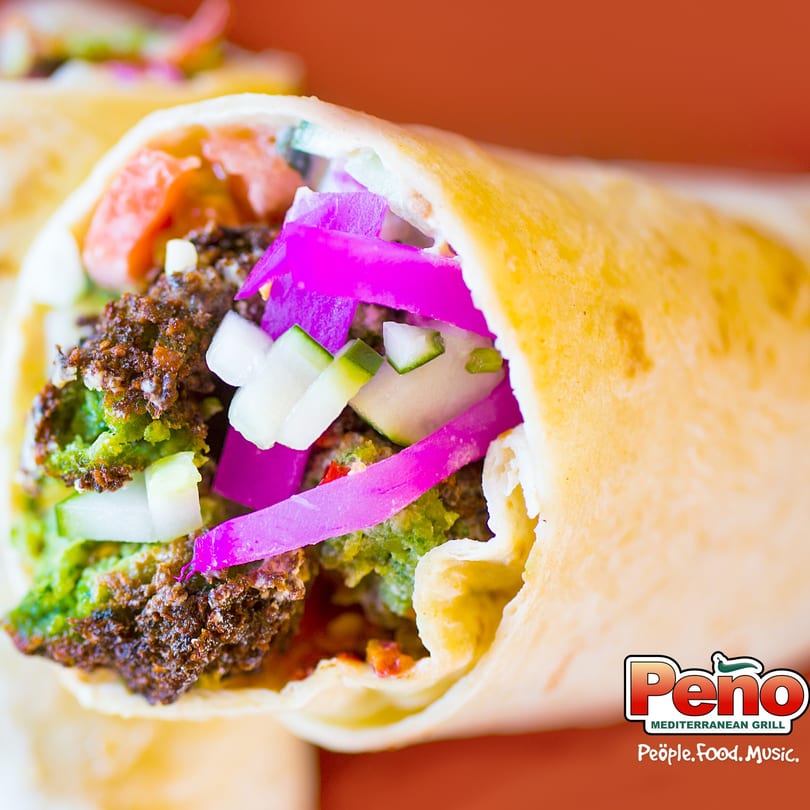 Close-up of a Peno Mediterranean Grill falafel wrap with vibrant pickled onions and fresh vegetables.