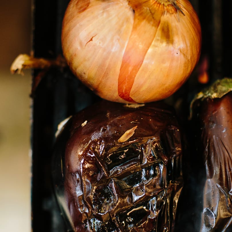 A whole onion sits atop a charred eggplant, ready for Mediterranean grilling.